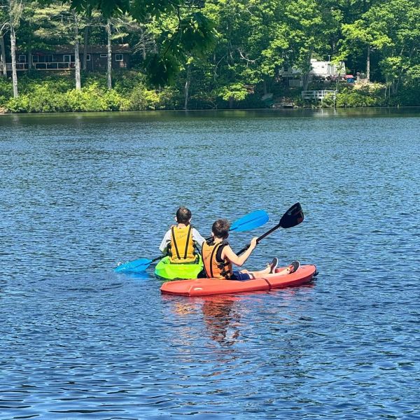 Two kids kayaking on a calm lake surrounded by trees.