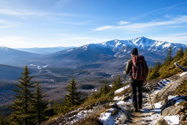 Hiker with backpack enjoying snowy mountain views on a clear day.