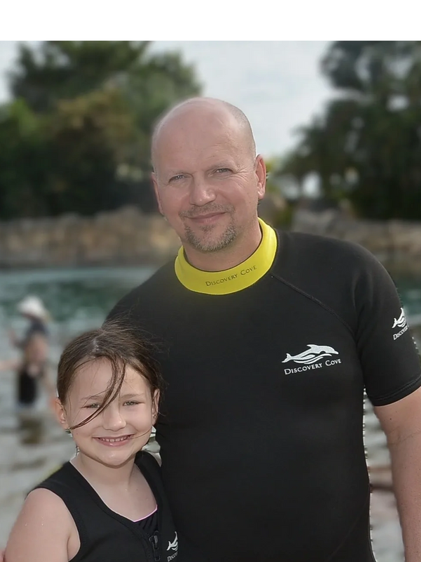 A man and a girl in wetsuits smile at the camera near water at Discovery Cove.