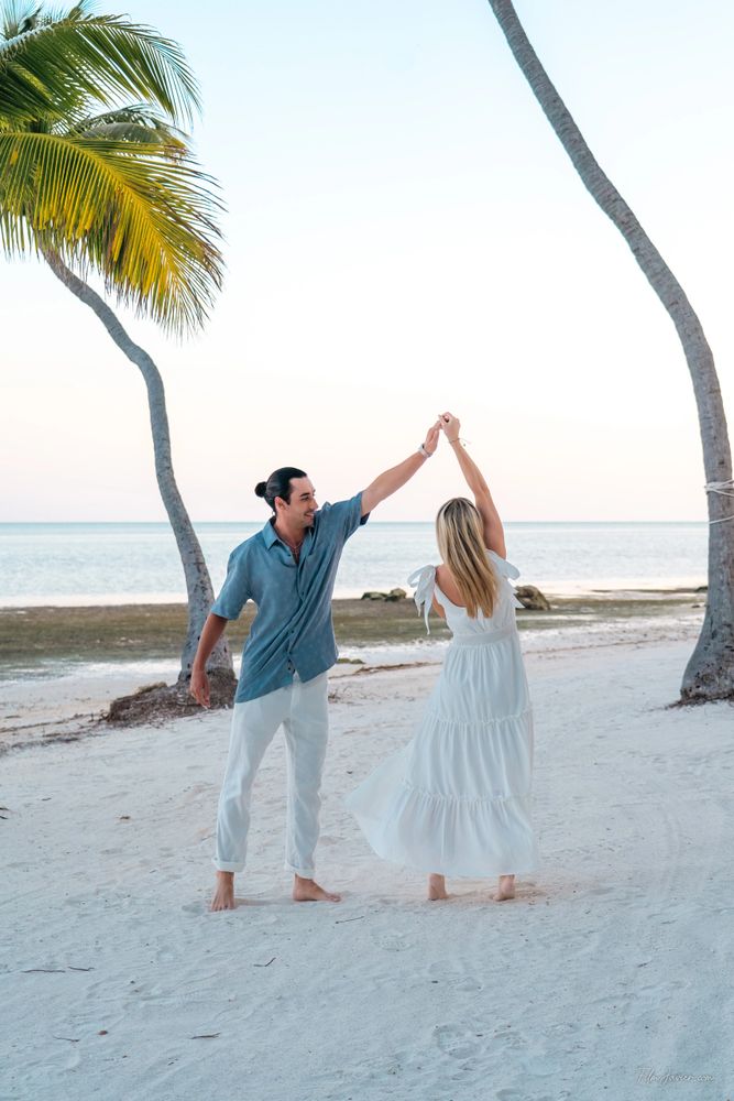 Couple dancing barefoot on a serene beach with palm trees.