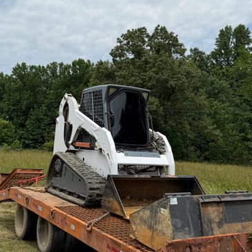 White compact loader on a trailer in a grassy area.