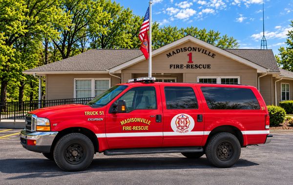 Red Madisonville Fire-Rescue truck parked outside the fire station.