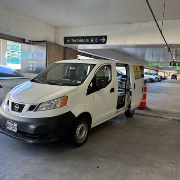 White Nissan van parked in an airport parking garage.