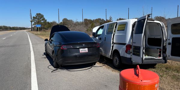 A black Tesla with its hood open on the roadside.