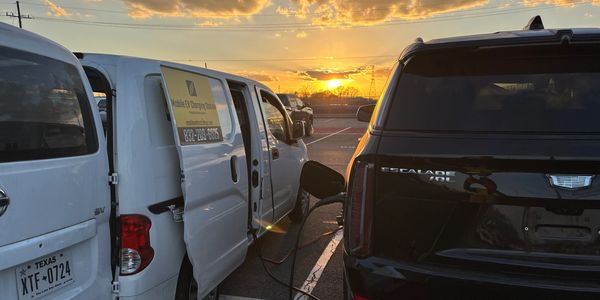 Sunset with one mobile charging van charging a Cadillac Escalade EV electric car.