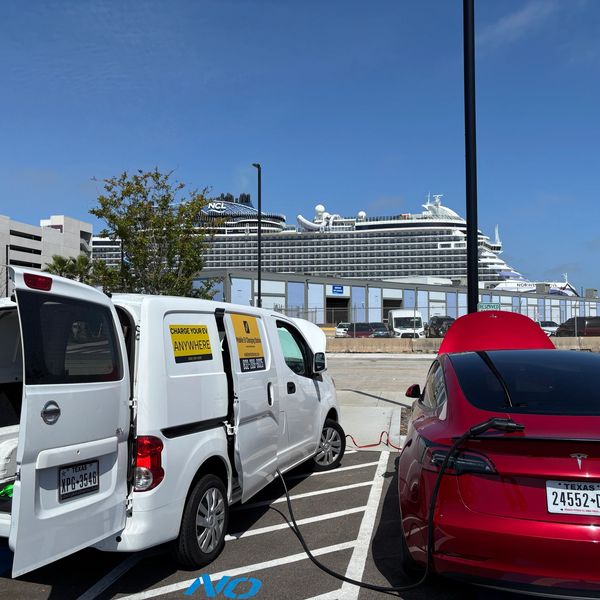 Electric vehicle charging in a parking lot with a cruise ship in the background in Galveston Texas.