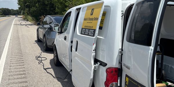 Electric vehicle charging on roadside by service van.