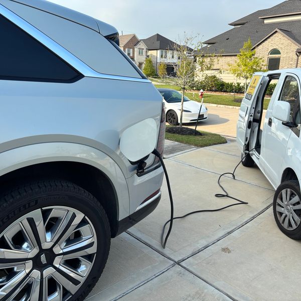 Silver Cadillac Escalade IQ electric car charging from a mobile EV charger white van in a residentia