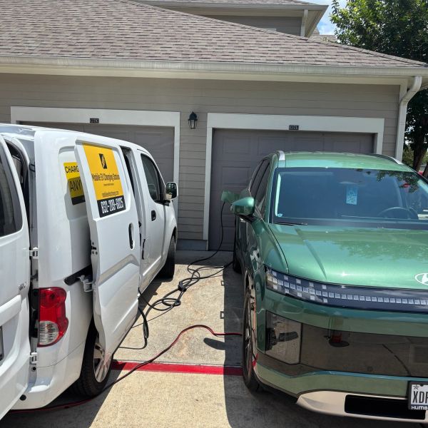Electric vehicle charging between a white van and green car.