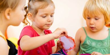 Three children engaged in a craft activity, focusing on a heart-shaped item.