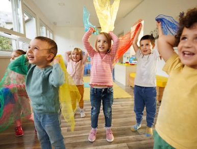 Children happily playing with colorful scarves indoors.