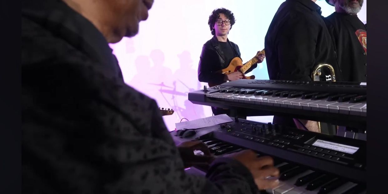 A band performs with keyboard, guitar, and brass instruments on stage.