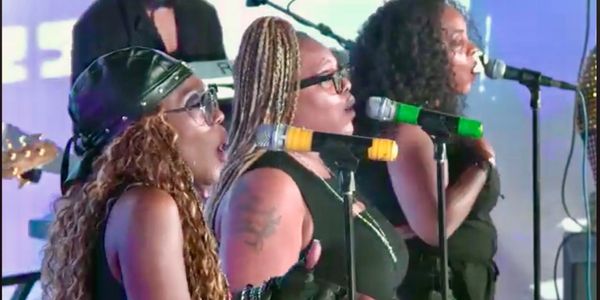 Three female singers passionately performing on stage with microphones.