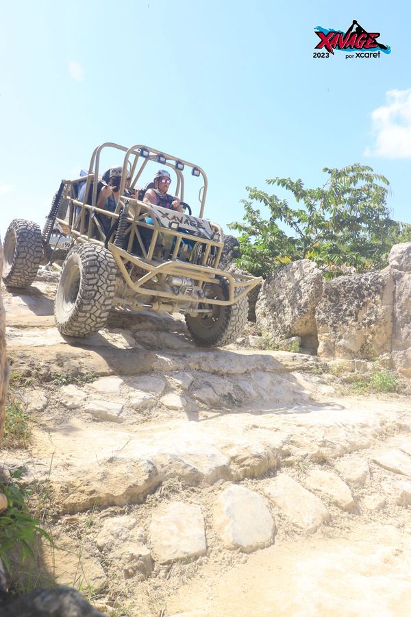 Adventure vehicle descending rocky terrain with two passengers wearing helmets.