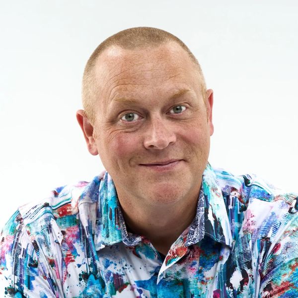 Smiling man wearing a colorful, patterned shirt against a white background.