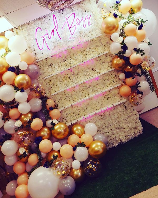Decorative balloon wall with 'Girl Boss' neon sign and floral backdrop.
