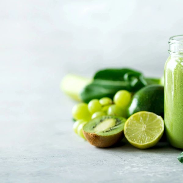 Green smoothie in jar surrounded by fresh green fruits and vegetables.