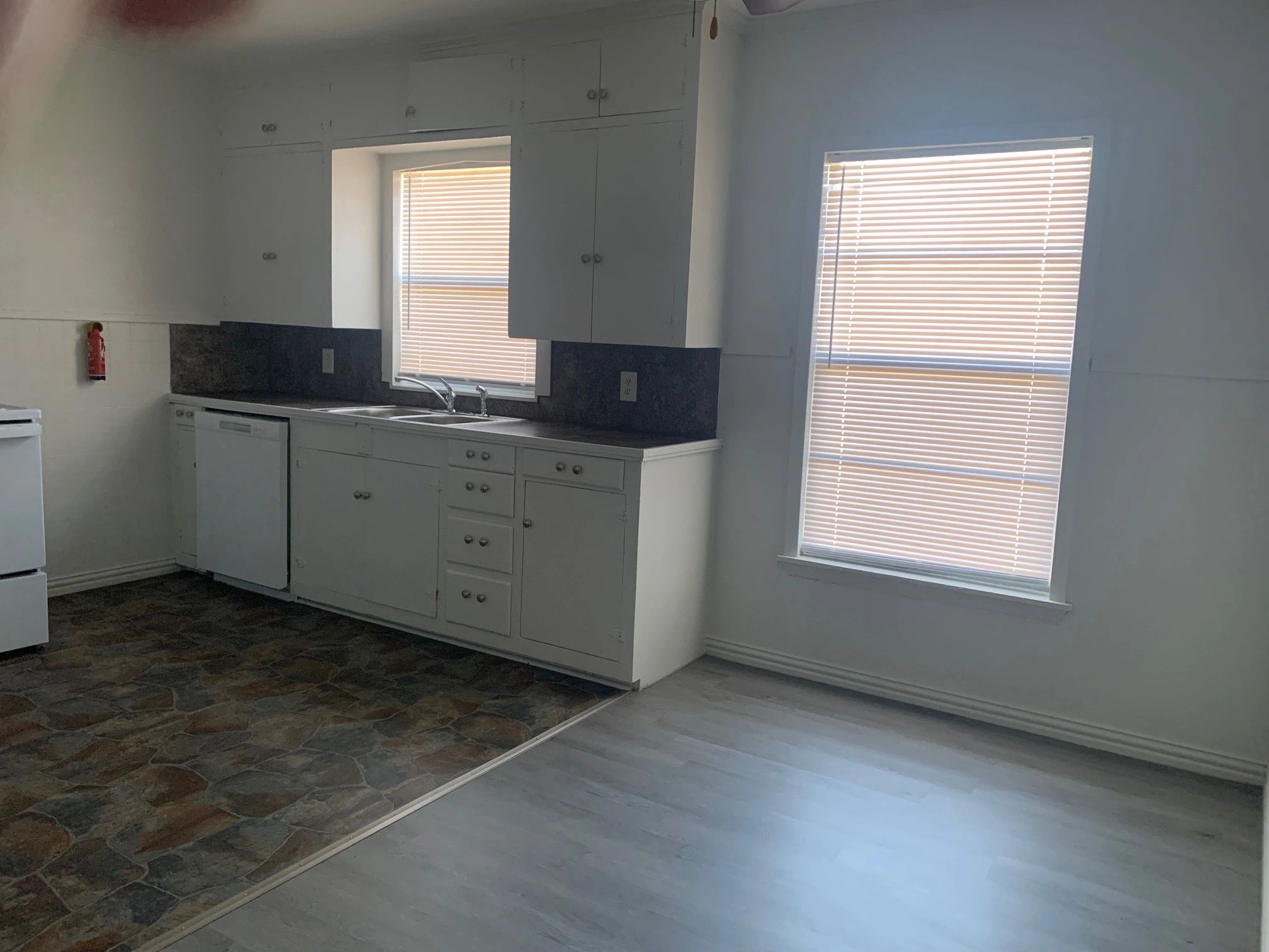 Simple kitchen with white cabinets and two windows with blinds.