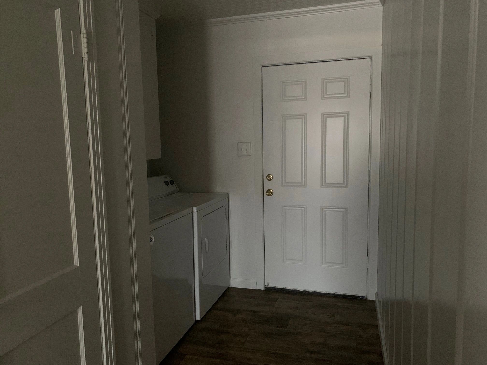 Dimly lit laundry room with washer, dryer, and white door.
