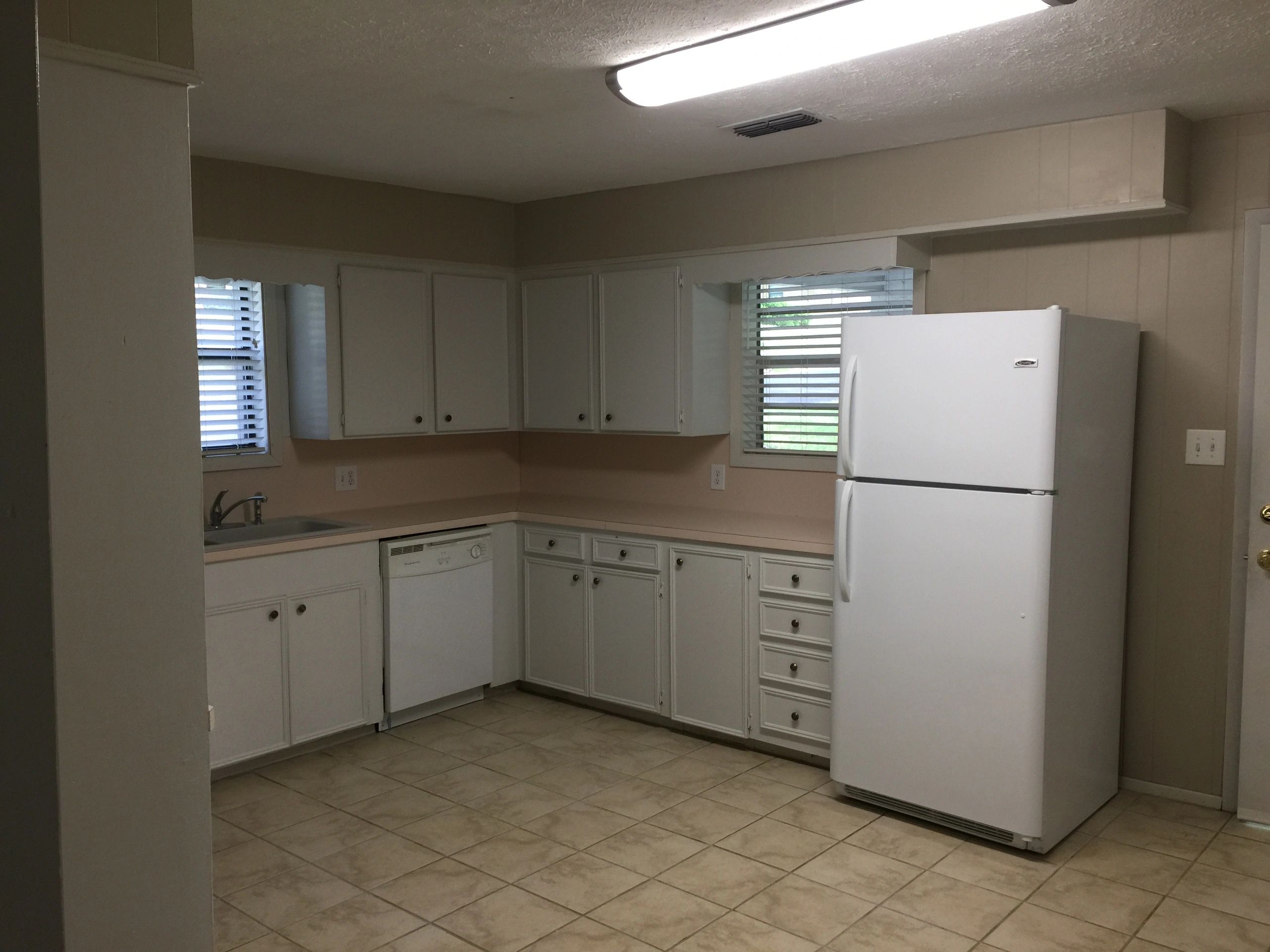 A simple kitchen with white cabinets, a white refrigerator, and tiled floor.