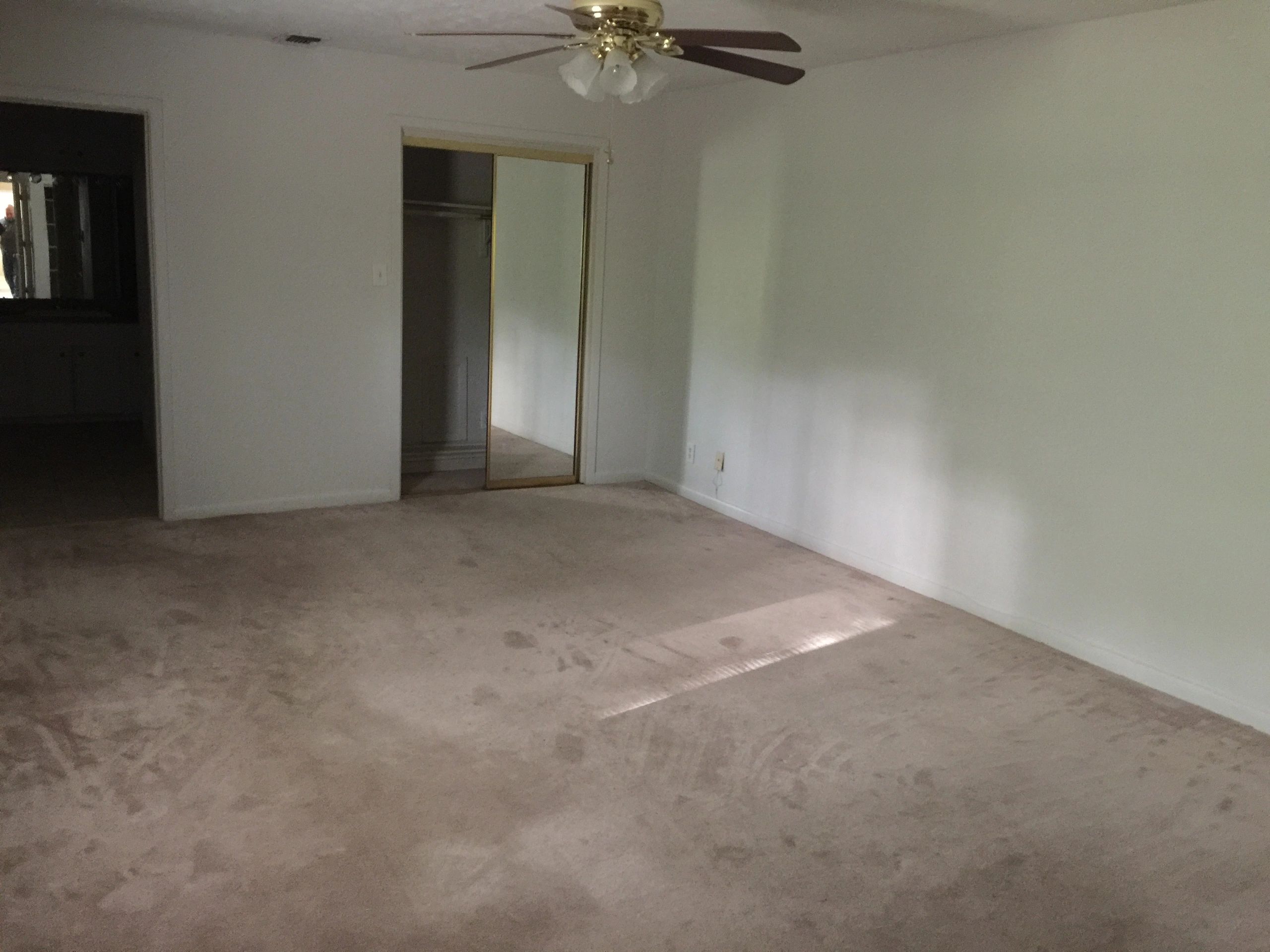 Empty room with beige carpet, white walls, ceiling fan, and mirrored closet door.