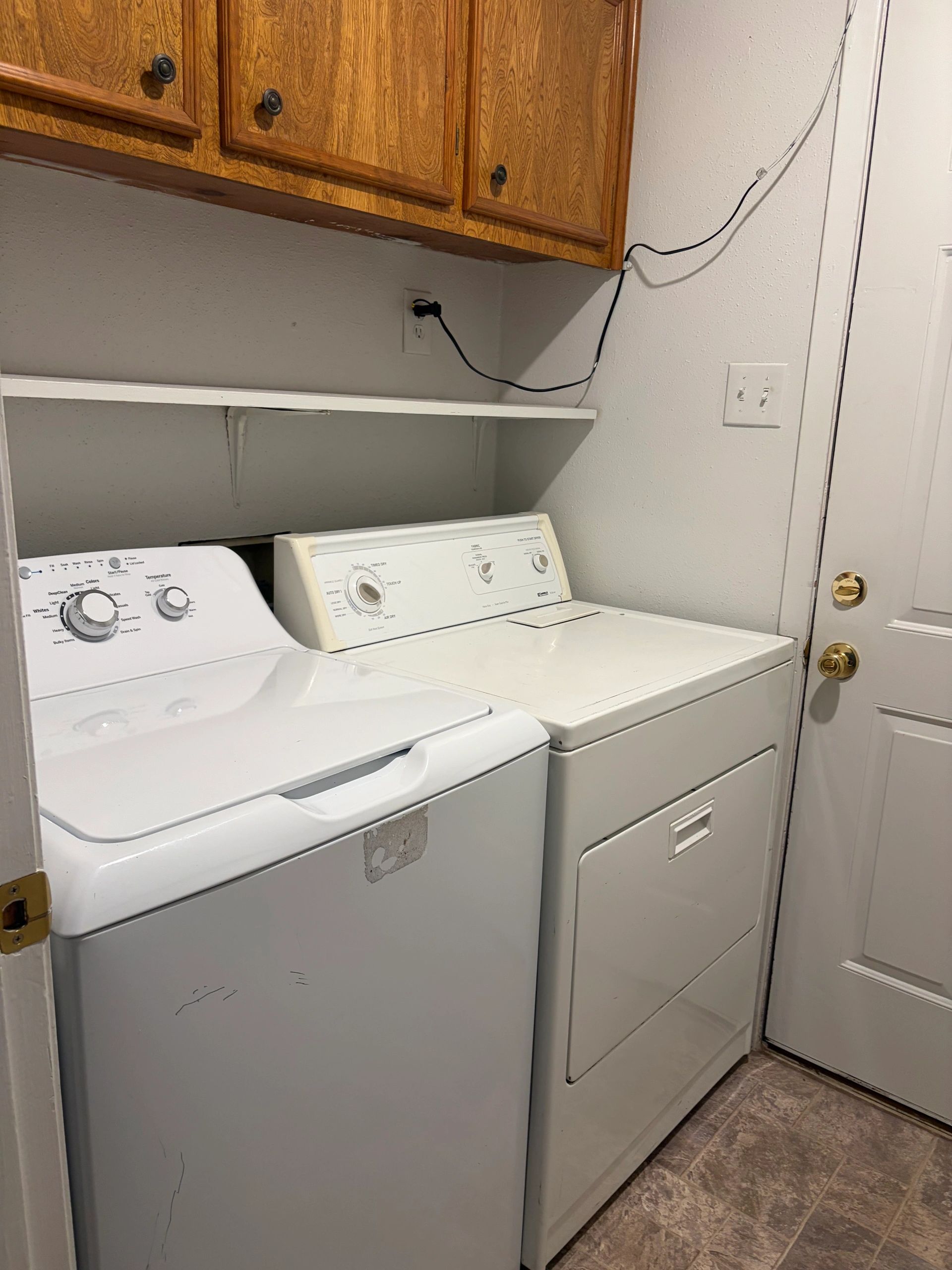 Laundry room with washing machine, dryer, and wooden cabinets.
