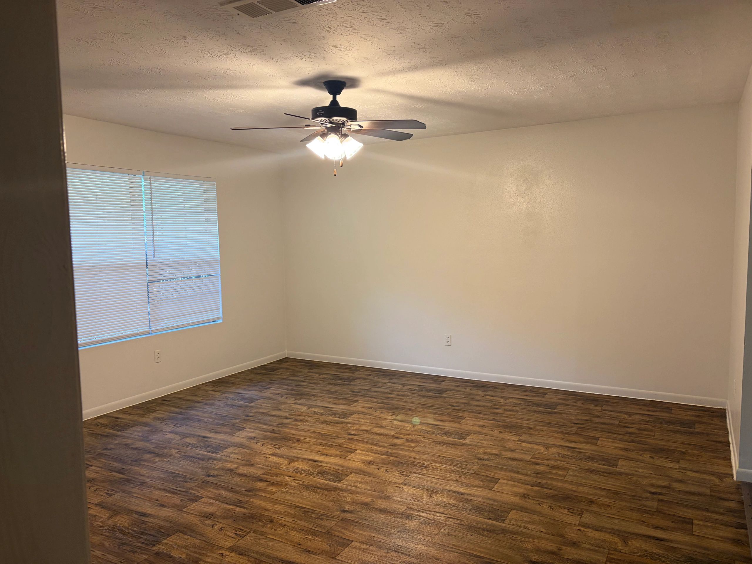Empty room with wooden floor, white walls, and ceiling fan light.
