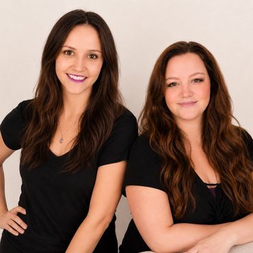 Two smiling women with long brown hair wearing black tops posing together.