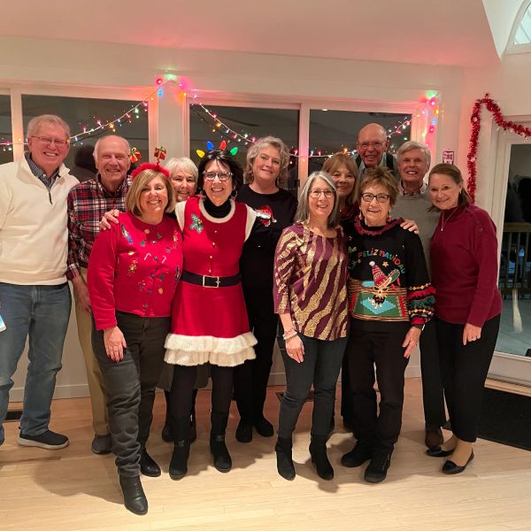 Group of older adults in festive holiday sweaters posing indoors.