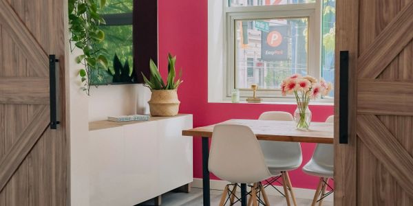 Bright dining nook with pink accent wall and white chairs seen through sliding barn doors.