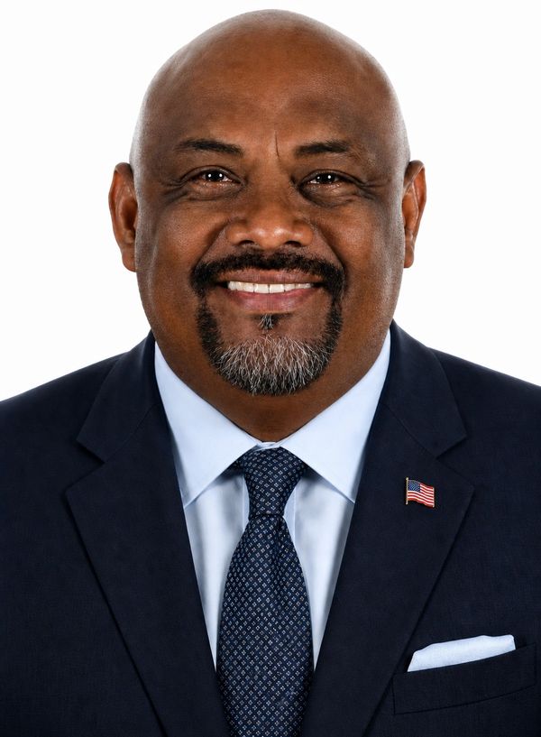 Smiling man in a dark suit with an American flag pin.