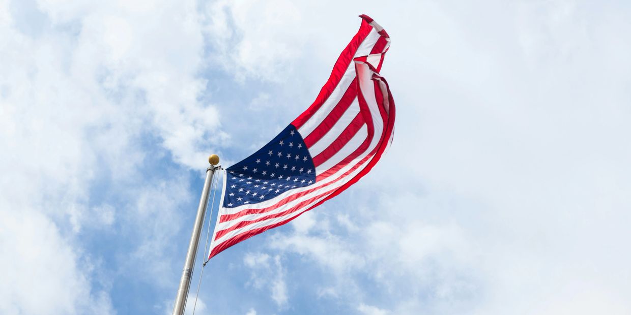 American flag waving against a partly cloudy sky.