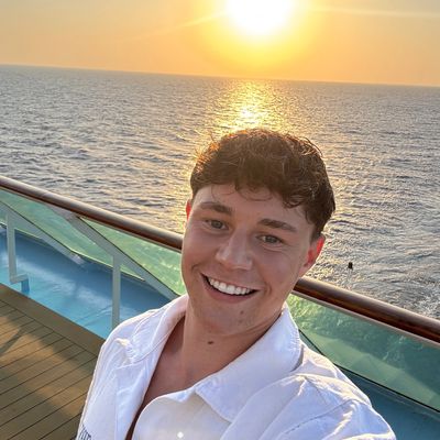 Young man smiling on ship deck at sunset.
