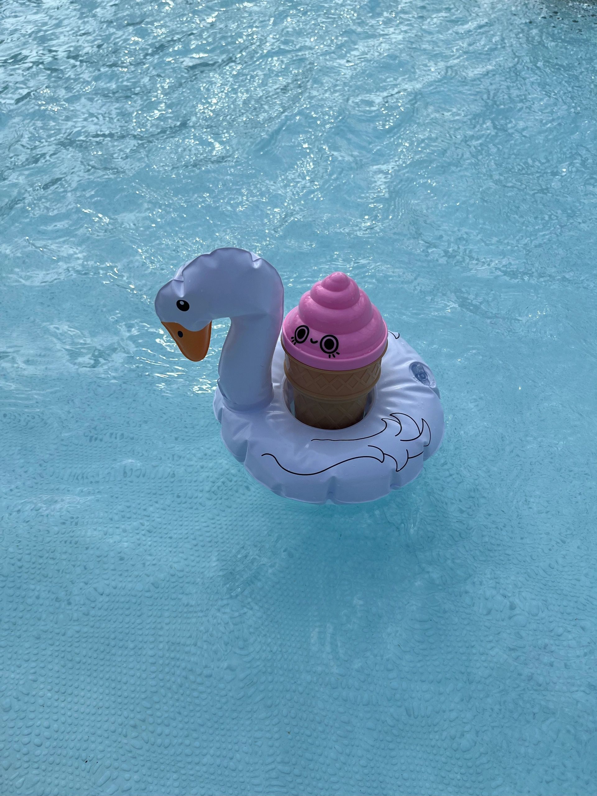 A cute inflatable swan with a pink ice cream float in a pool.