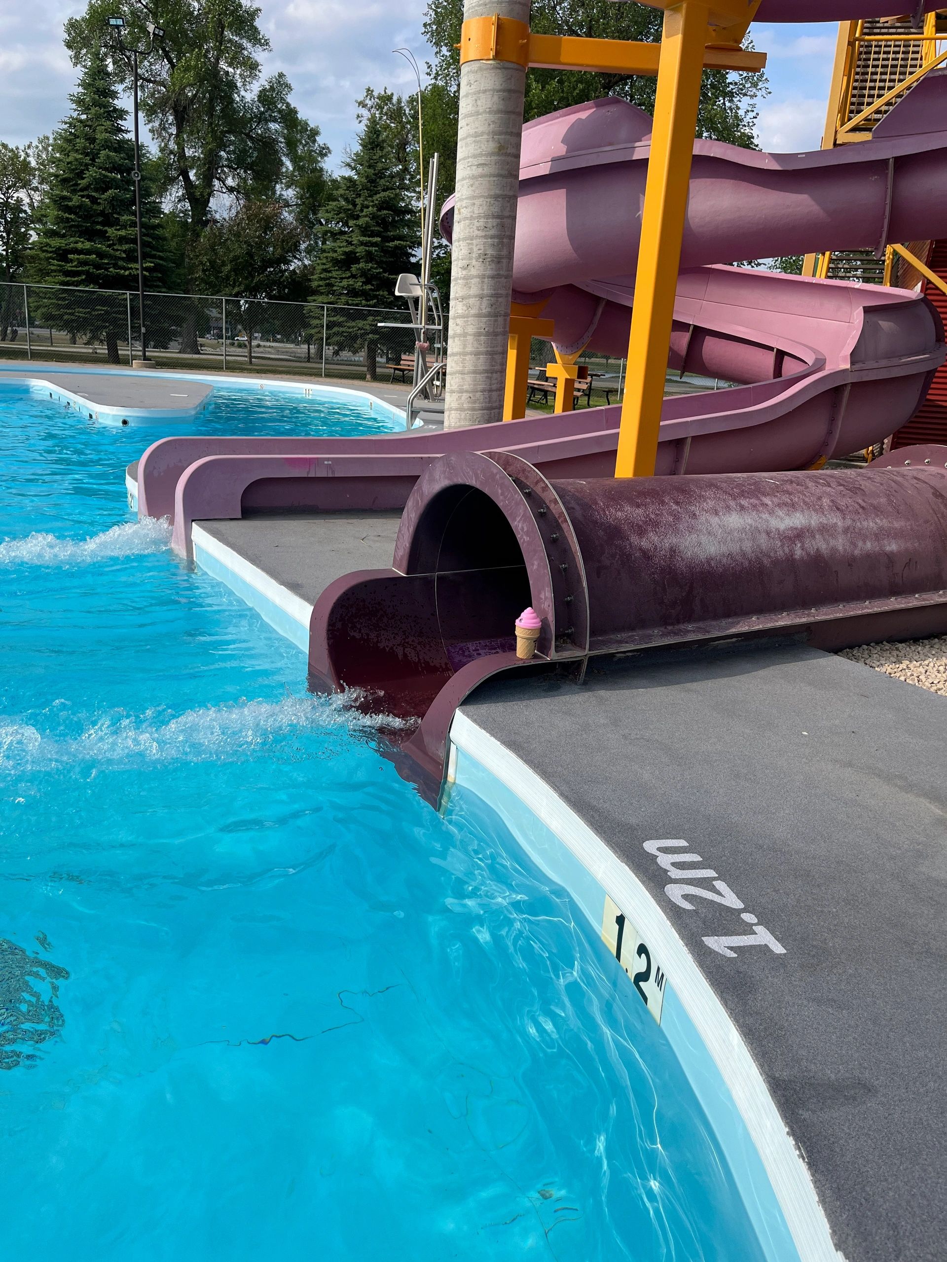 Purple water slide at a pool with an ice cream cone decoration at the exit.
