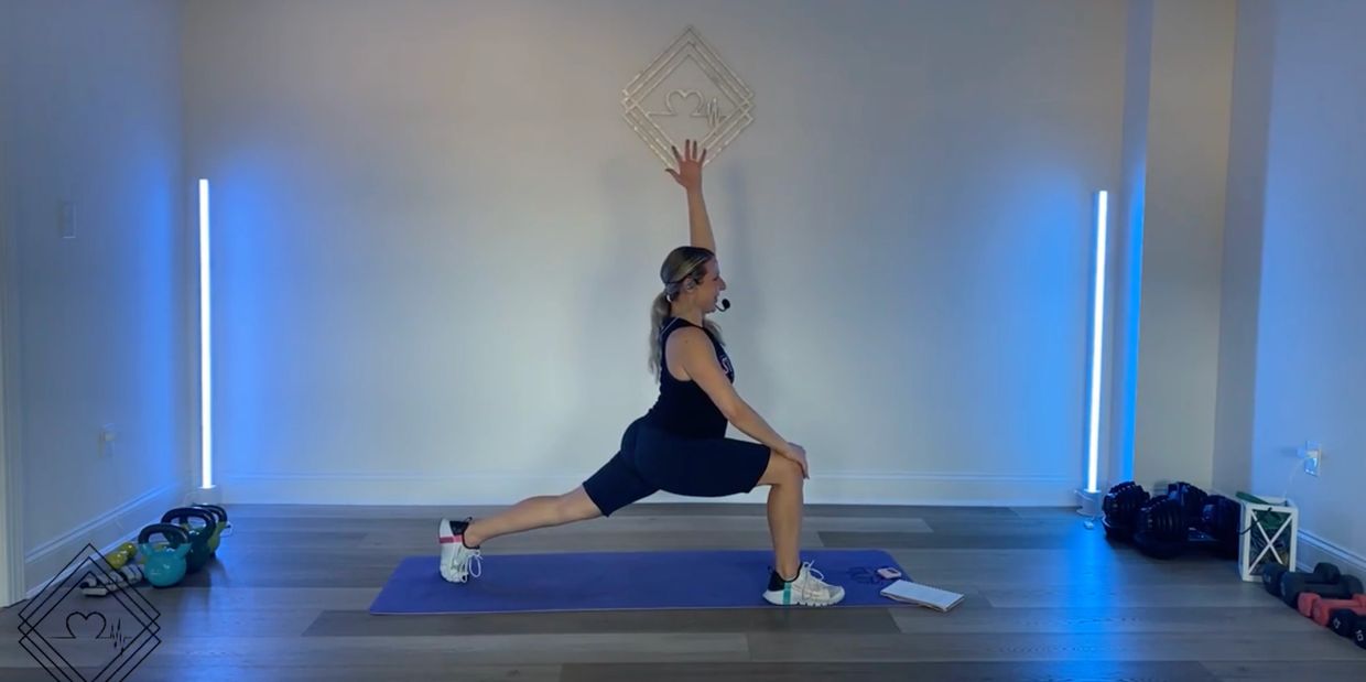 Woman performing a lunge stretch on a yoga mat in a well-lit room.