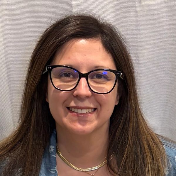 Smiling woman with long brown hair and black glasses.