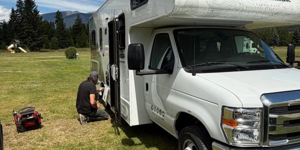 Man working on a white RV in a grassy area.