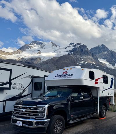 Truck camper parked near snowy mountains under blue sky.