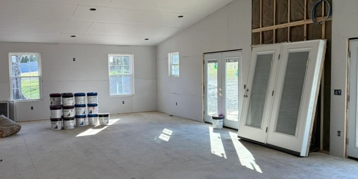 Spacious room under construction with drywall and stacked paint buckets.