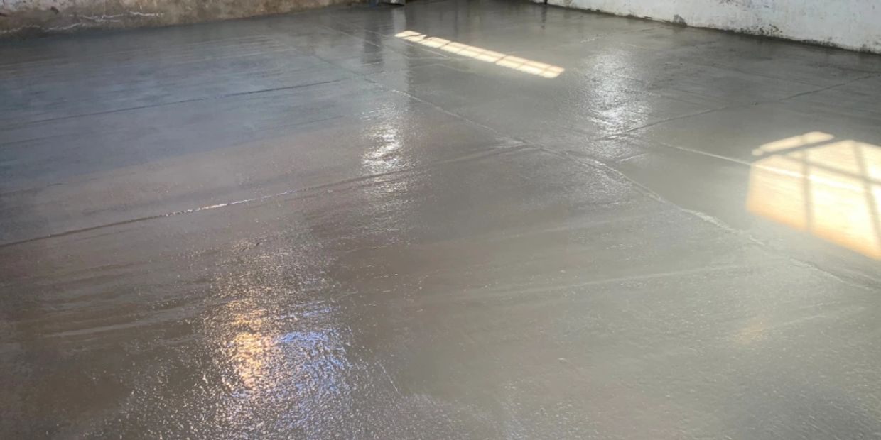 Newly poured, smooth concrete floor reflecting window light in an unfinished room.