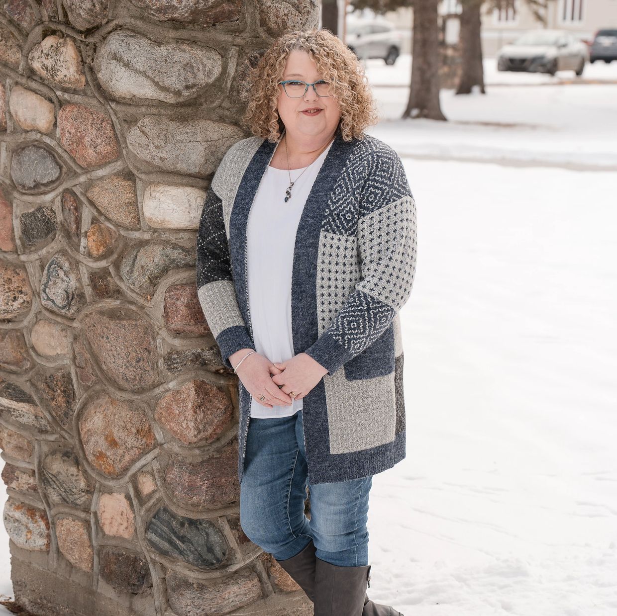 Beverley, an End-of-Life Doula, is leaning against an old stone pillar at St. Albert Parish, AB,  CA