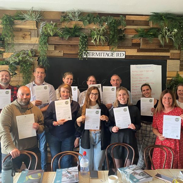 12 learners smiling at the camera, standing in two lines, holding their MHFA certifcates.