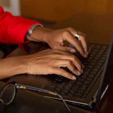Person typing on a laptop keyboard with glasses nearby.