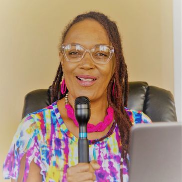 Woman smiling with microphone and colorful attire, speaking confidently.