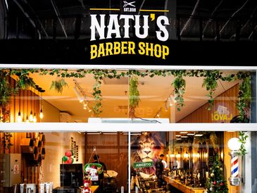 Exterior view of Natu's Barber Shop with warm lighting and greenery.