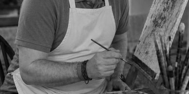 An artist painting on a canvas with a brush, wearing an apron.