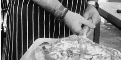 Chef slicing a freshly baked pizza on a wooden board.