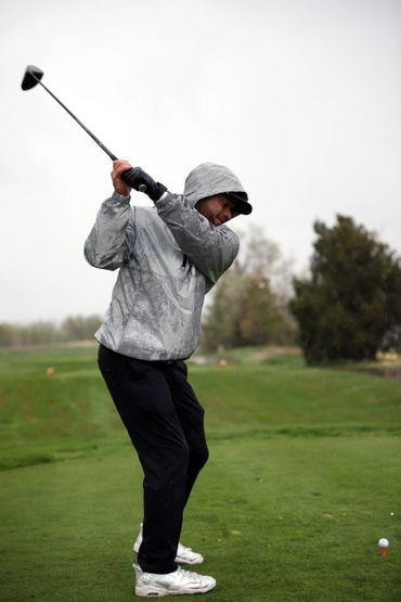 Golfer in a rain jacket preparing to swing on a wet golf course.