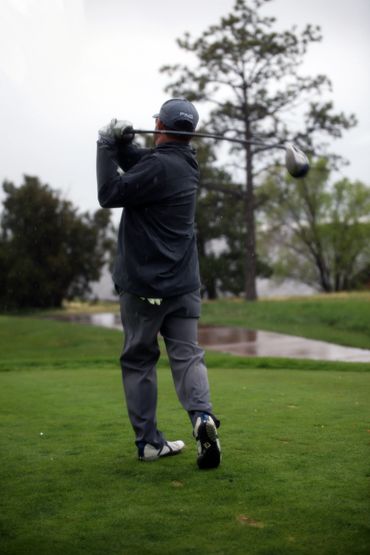 Golfer finishing a swing on a rainy golf course.